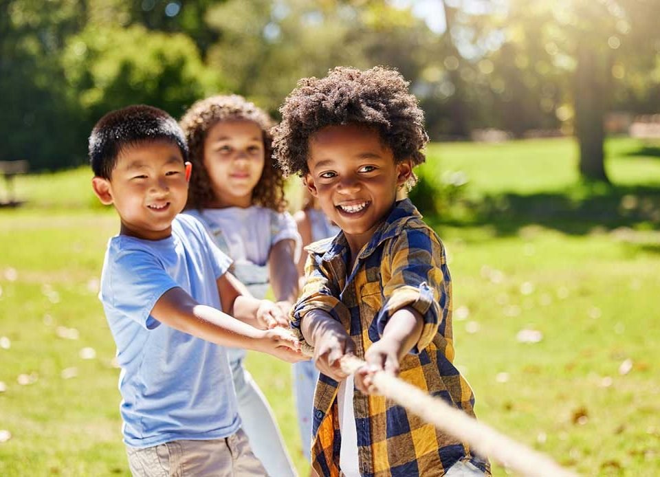 Fun, games and kids playing tug of war together outdoor in a park or playground in summer. Friends, diversity and children pulling a rope while being playful fun or bonding in a garden on a sunny day.