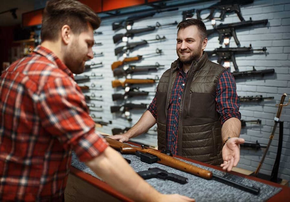 Man and owner choosing rifle in gun shop. Euqipment for hunters on stand in weapon store, hunting and sport shooting hobby