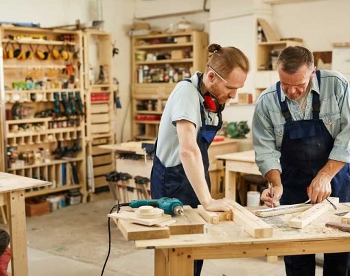 Portrait of two carpenters working with wood standing at table in workshop, copy space