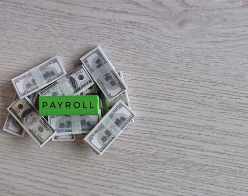 Wooden cube with text PAYROLL on top of banknotes. Business and financial concept