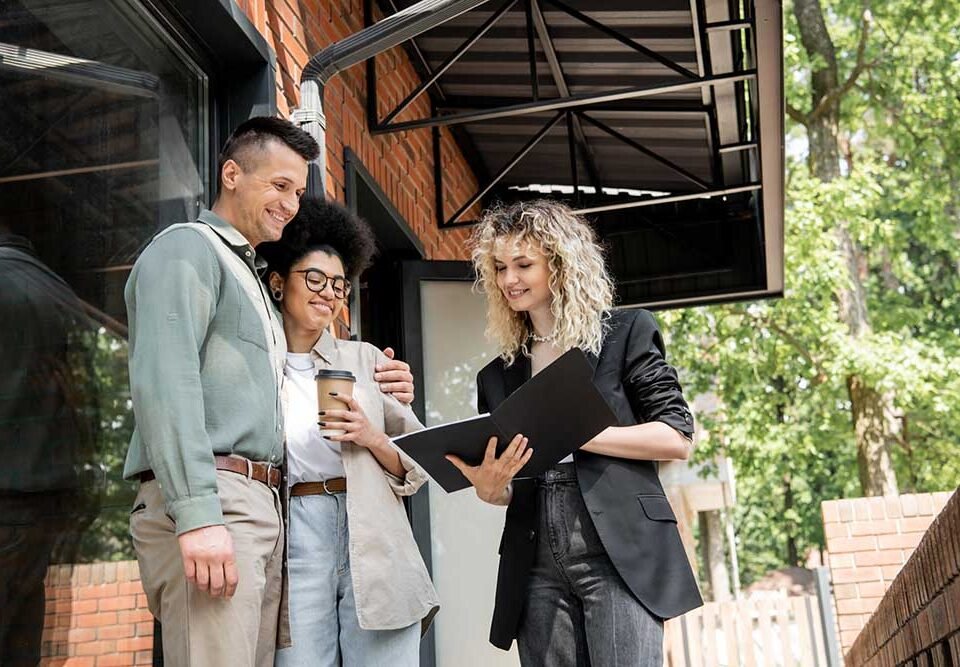 smiling real estate agent showing documents to interracial coupl