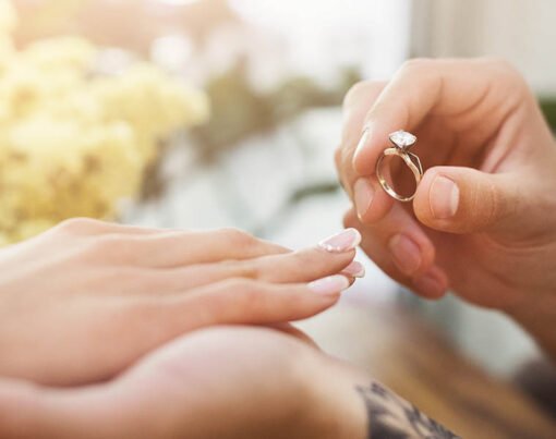 She said YES. Man putting on his girlfriends finger engagement ring, sitting on romantic dinner at cafe. Wedding proposal concept, copy space